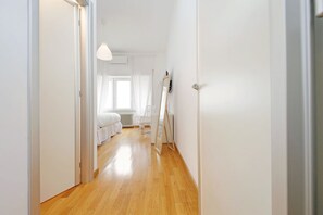 Un estrecho pasillo con suelo de madera que conduce a un dormitorio con cama, radiador y ventana.