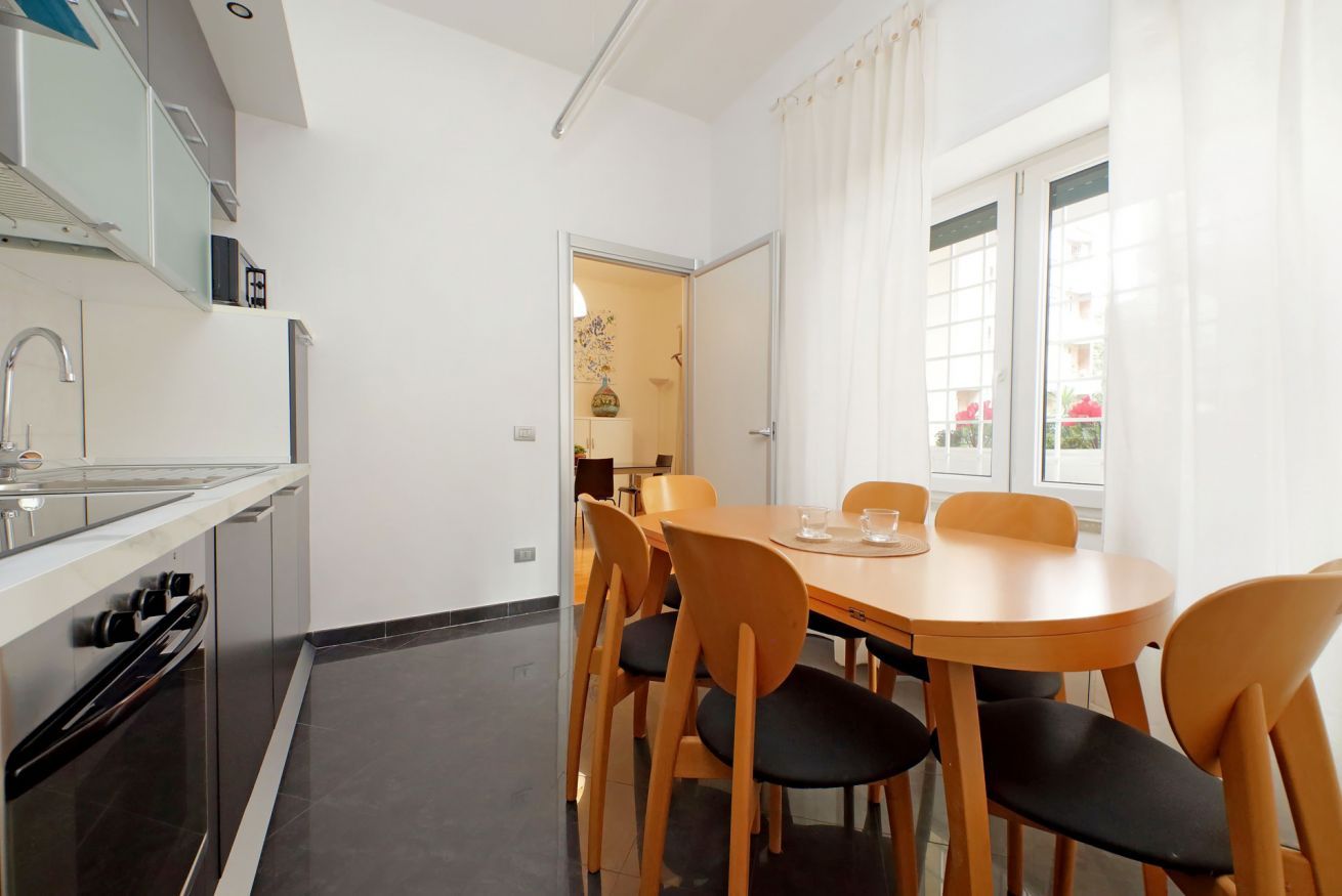 Uma cozinha moderna com área de refeições, incluindo uma mesa redonda e cadeiras, e vista através de uma porta aberta.