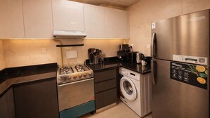Une cuisine compacte équipée d’une cuisinière à gaz, d’un lave-linge encastré, d’un réfrigérateur en acier inoxydable et d’un four à micro-ondes.