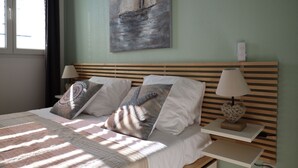A neatly made bed with a striped blanket, two pillows, a bedside table with a lamp, and a wall painting of a sailboat. - 300 m from beach. Comfort, terrace, wifi, bed linen, garden, swimming pool, parking lot (Moliets-et-Maa)