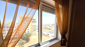 Ein Fenster mit Vorhängen, Blick auf ein Wohngebiet mit Gebäuden und einer unbefestigten Straße.