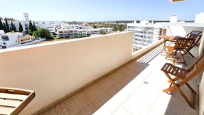 Ein Balkon mit Tisch und Stühlen, der auf einen Küsten-Stadtpanoramablick bietet, mit modernen Gebäuden.
