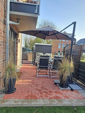 Eine Terrasse mit Pflasterboden, einem Metallgrill und zwei Blumentöpfen.