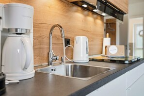Eine moderne Küche mit Spüle aus Edelstahl, einer Kaffeemaschine und einem Wasserkocher.