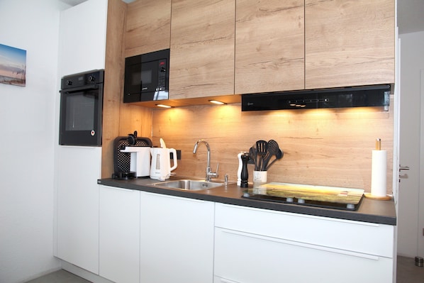 Eine moderne Küche mit weißen Schränken, einem schwarzen Backofen, einer Mikrowelle und einer Holzrückwand.