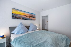 Ein Schlafzimmer mit Bett, Kissen, einem Nachttisch mit Lampe, einem Wandbild und einer Tür.