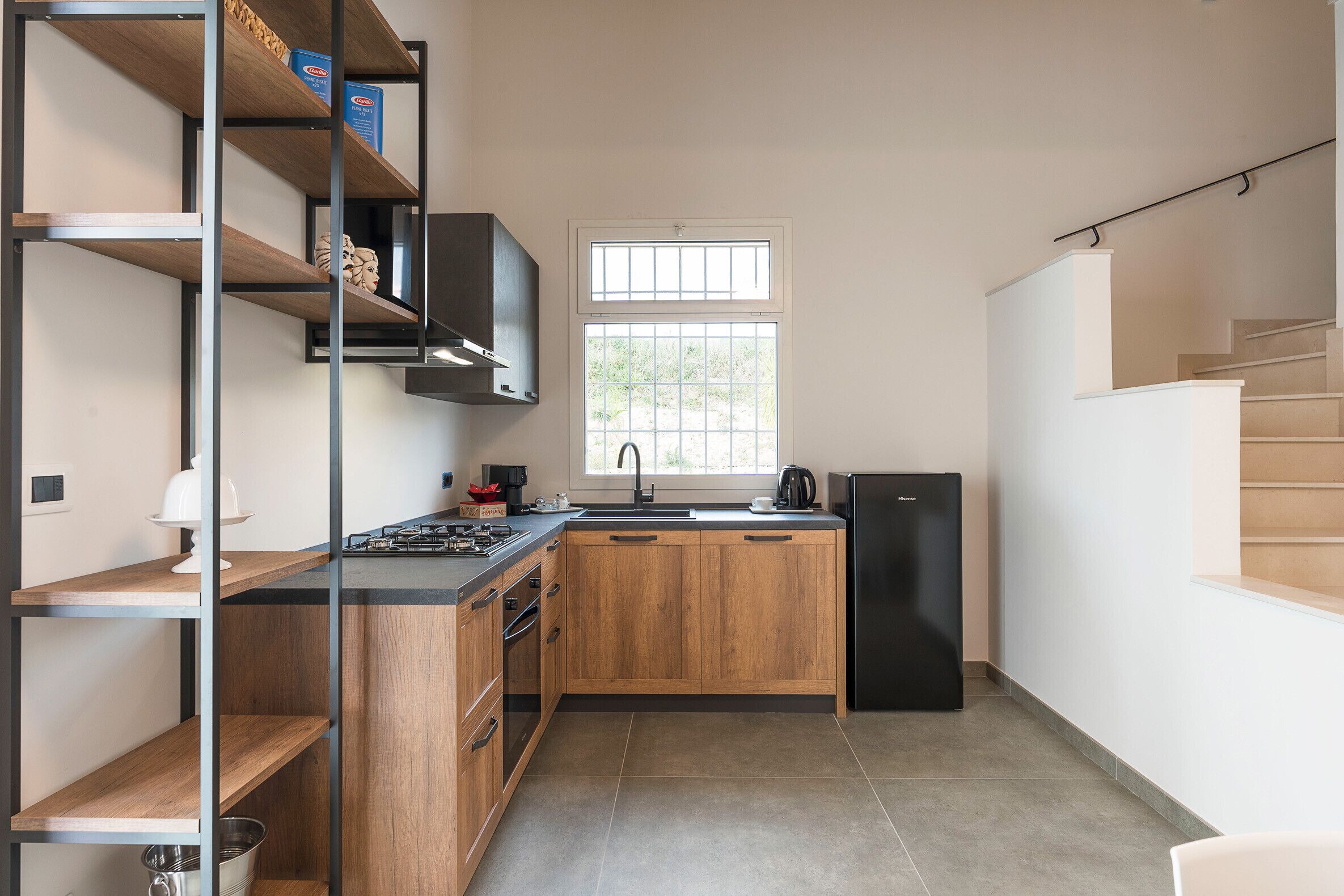 Een moderne keuken met houten kastjes, een zwarte koelkast en een raam boven de gootsteen.