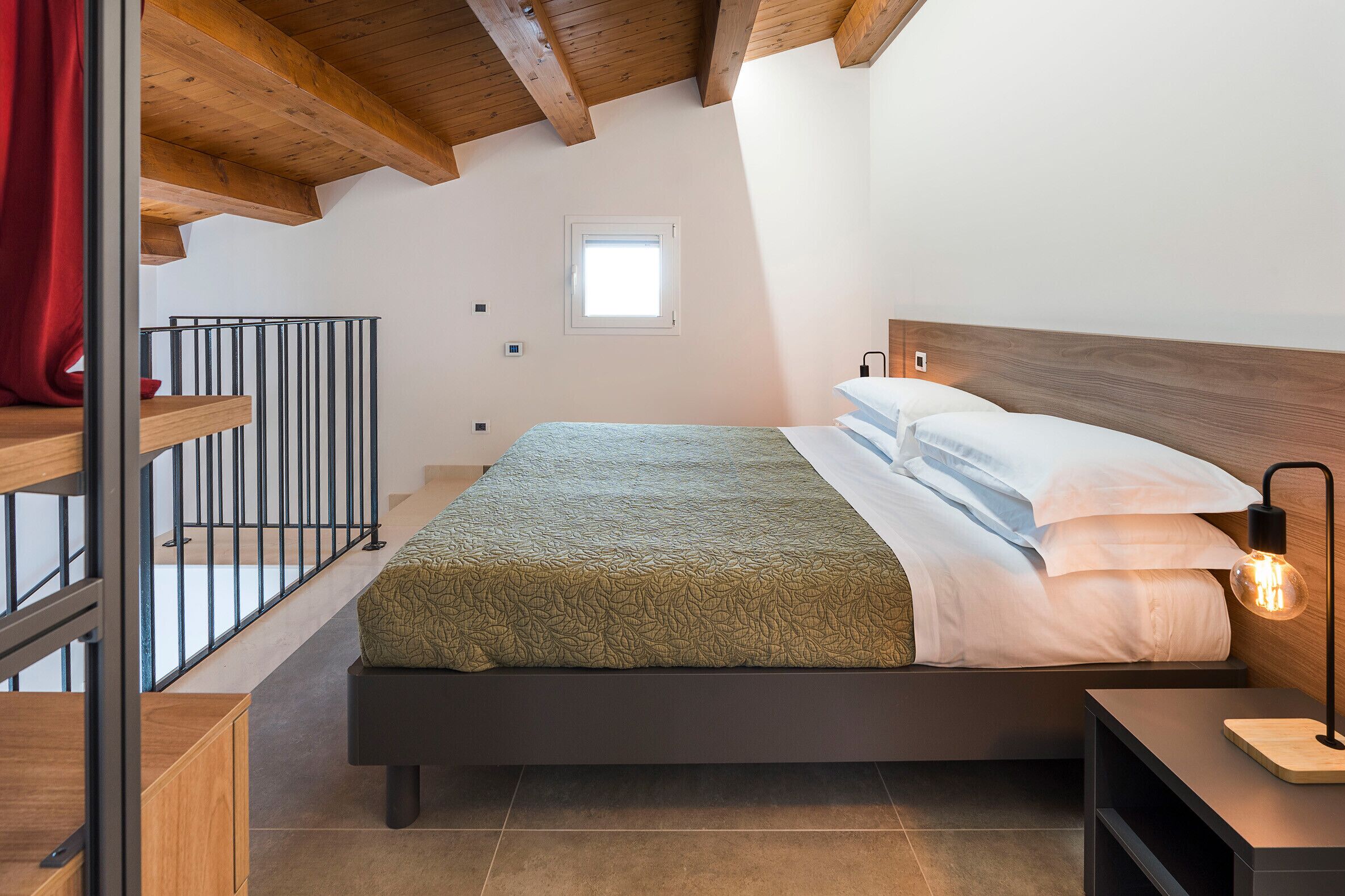 Una camera da letto con un letto, travi in legno a soffitto, una finestra e un comodino con una lampada.