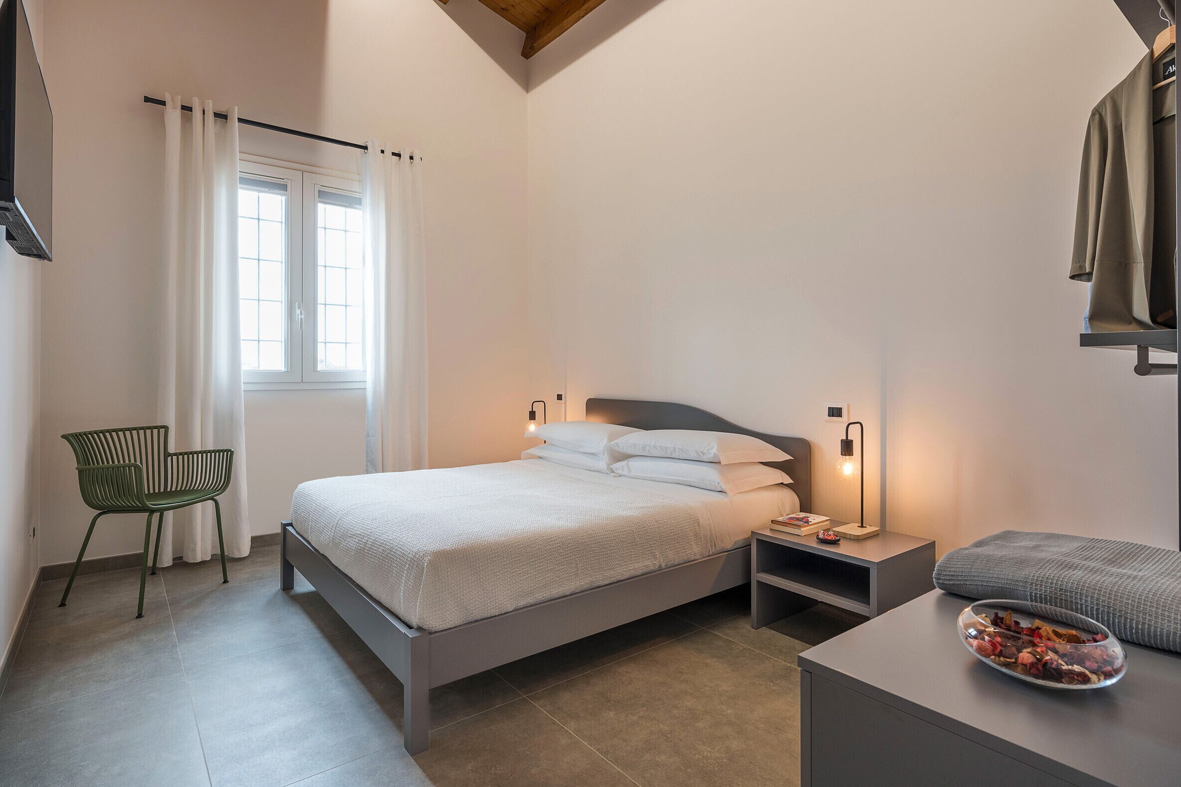 Ein modernes Schlafzimmer mit einem Bett, Nachttischen, einem Sessel und einem Fenster mit Vorhängen.