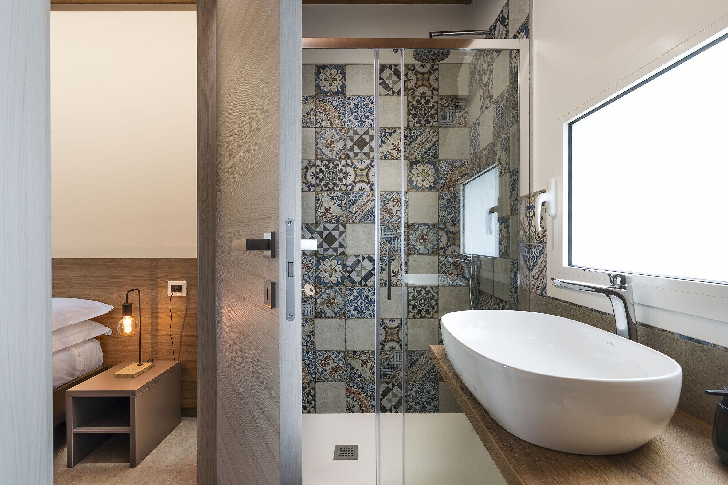 Ein modernes Badezimmer mit einem großen weißen Waschbecken, einer Duschkabine aus Glas und einer Fliesenrückwand mit Muster.