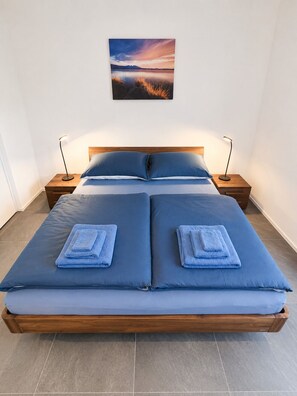 Un lit double avec une literie et des oreillers bleus, deux tables de chevet avec des lampes et un tableau encadré au mur.