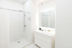 Ein modernes Badezimmer mit barrierefreier Dusche, einem großen Spiegel und einem weißen Waschtisch mit Schubladen.