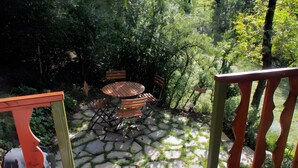 Une terrasse avec une table ronde et des chaises, entourée de dalles de pierre et de verdure.