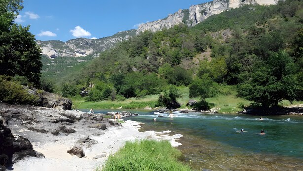 Une rivière aux eaux claires, bordée d’un paysage rocheux et de verdure.