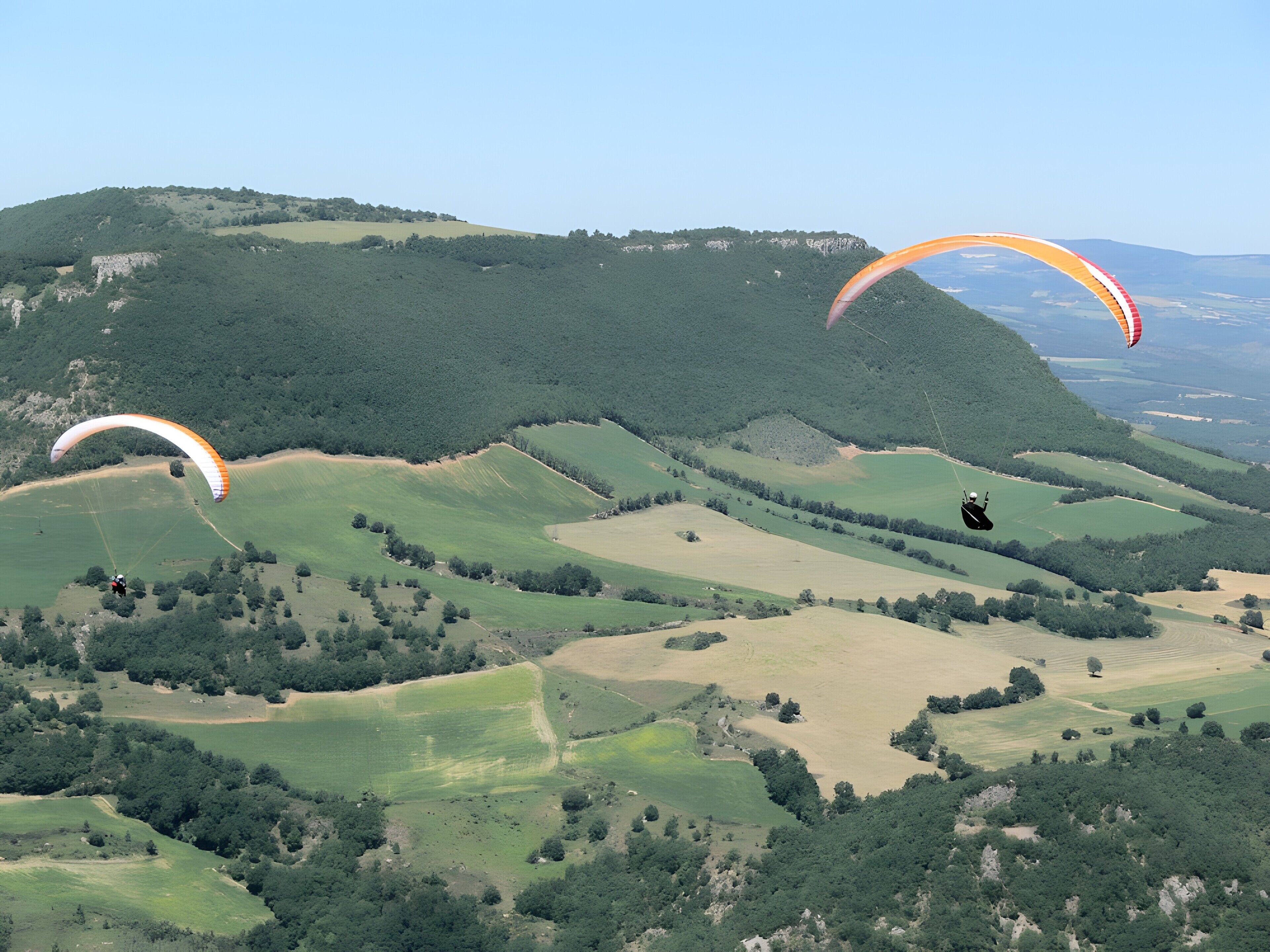 A landscape with rolling hills and two paragliders.