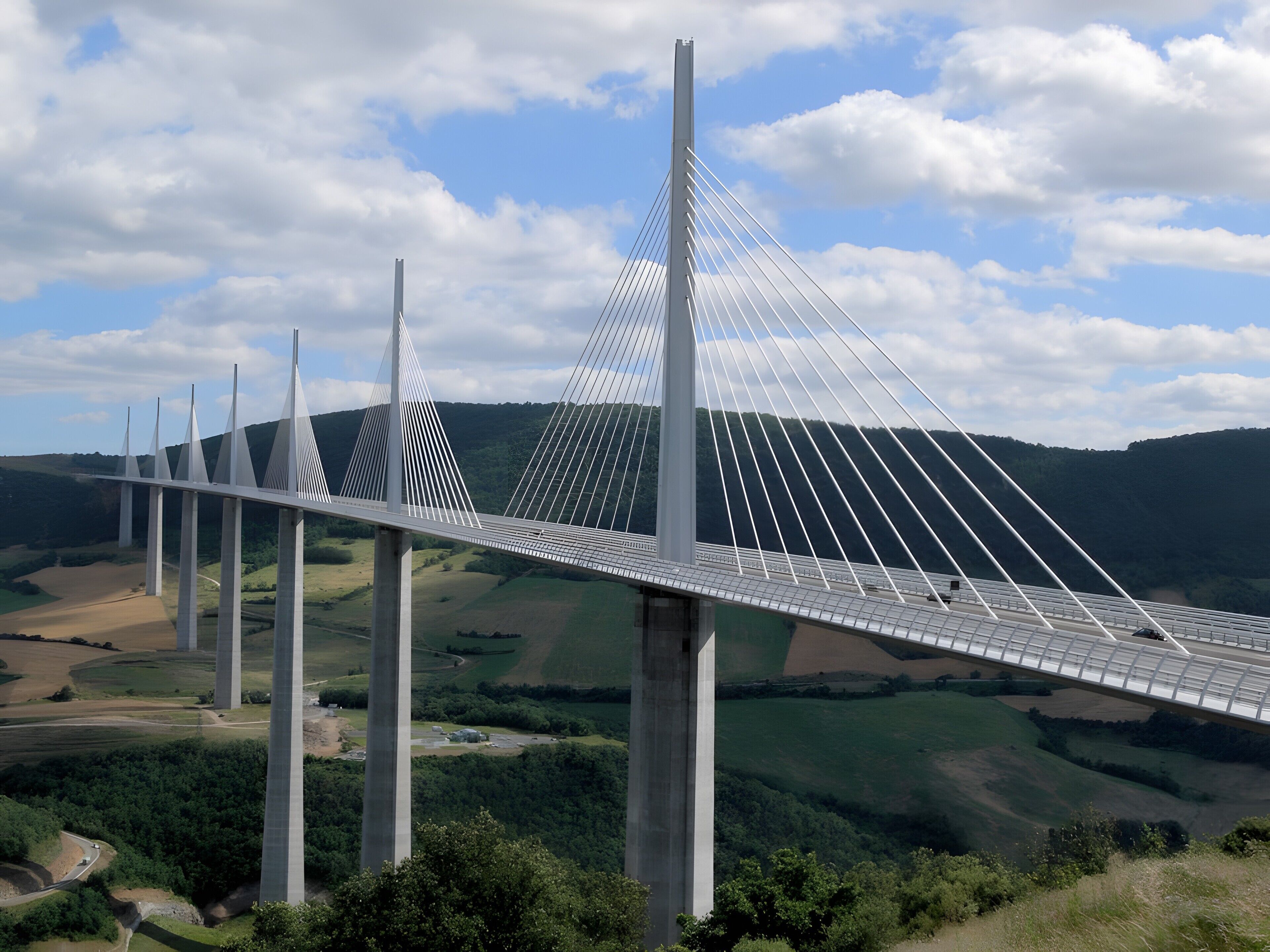 Un puente atirantado con múltiples torres, que cruza un valle con colinas verdes y un cielo despejado.