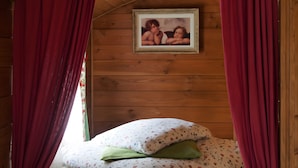 Une pièce de style cabane en bois, avec un lit, des rideaux rouges et un tableau encadré au mur.