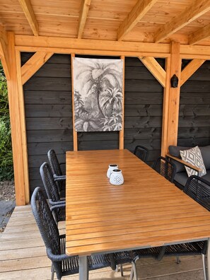 A covered outdoor dining area with a wooden table and black wicker chairs. - Boslodge 't Wims, a lovely chalet with a covered patio (Eext)