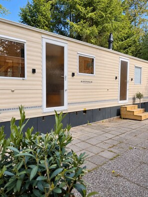 A mobile home with a sliding door, a small window, and a chimney. - Boslodge 't Wims, a lovely chalet with a covered patio (Eext)
