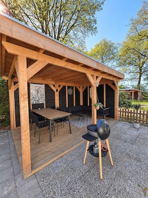An outdoor wooden pergola with a table and chairs, a barbecue grill, and a seating area.