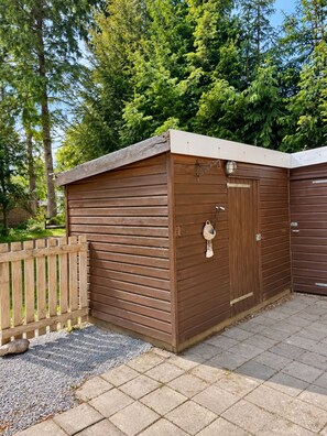 A wooden shed with a door and a small window, surrounded by a wooden fence and gravel. - Boslodge 't Wims, a lovely chalet with a covered patio (Eext)