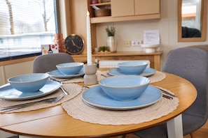 A round dining table with blue bowls and plates, a lit candle, and a clock on the wall.