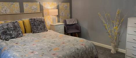 A bedroom with a bed, nightstand, chair, dresser, and a vase with branches.