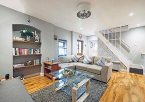 Una sala de estar con una mesa de centro de vidrio, un sofá color crema, una estantería y una escalera.