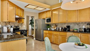A modern kitchen with wooden cabinets, granite countertops, stainless steel appliances, and a dining area with a round table and green chairs. - Spacious and cozy home in San Jose with a park view (San Jose)