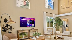 A spacious living room with a large flat-screen TV mounted on the wall, a comfortable seating area with sofas and chairs, a coffee table, and a potted plant. - Spacious and cozy home in San Jose with a park view (San Jose)