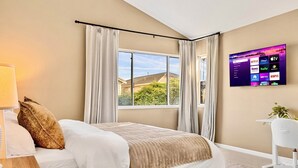 A bedroom with a bed, a desk, a chair, a TV mounted on the wall, and a window with curtains. - Spacious and cozy home in San Jose with a park view (San Jose)