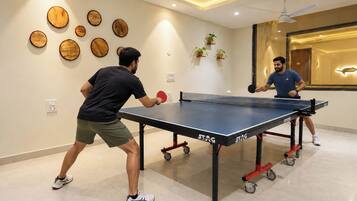 Due persone giocano a ping pong in una stanza con un tavolo da ping pong, decorazioni in legno a parete e piante in vaso.