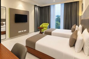 Una camera d'albergo con due letti, televisione, una sedia e una finestra con tende.