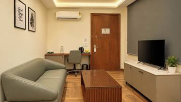 A modern office space with a sofa, a wooden coffee table, a desk with a chair, a television, and an air conditioning unit.