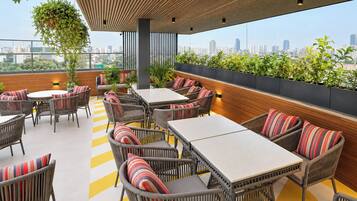 An outdoor seating area with wicker furniture and striped cushions, overlooking a cityscape.