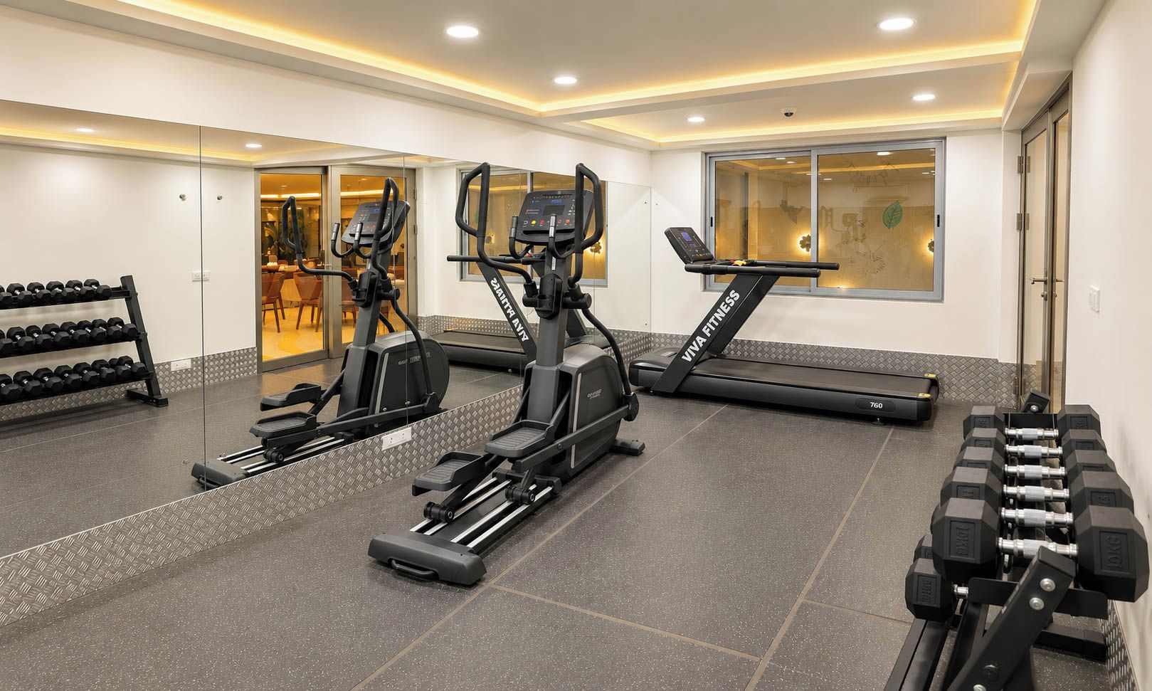 A gym with treadmills, elliptical machines, and dumbbells.