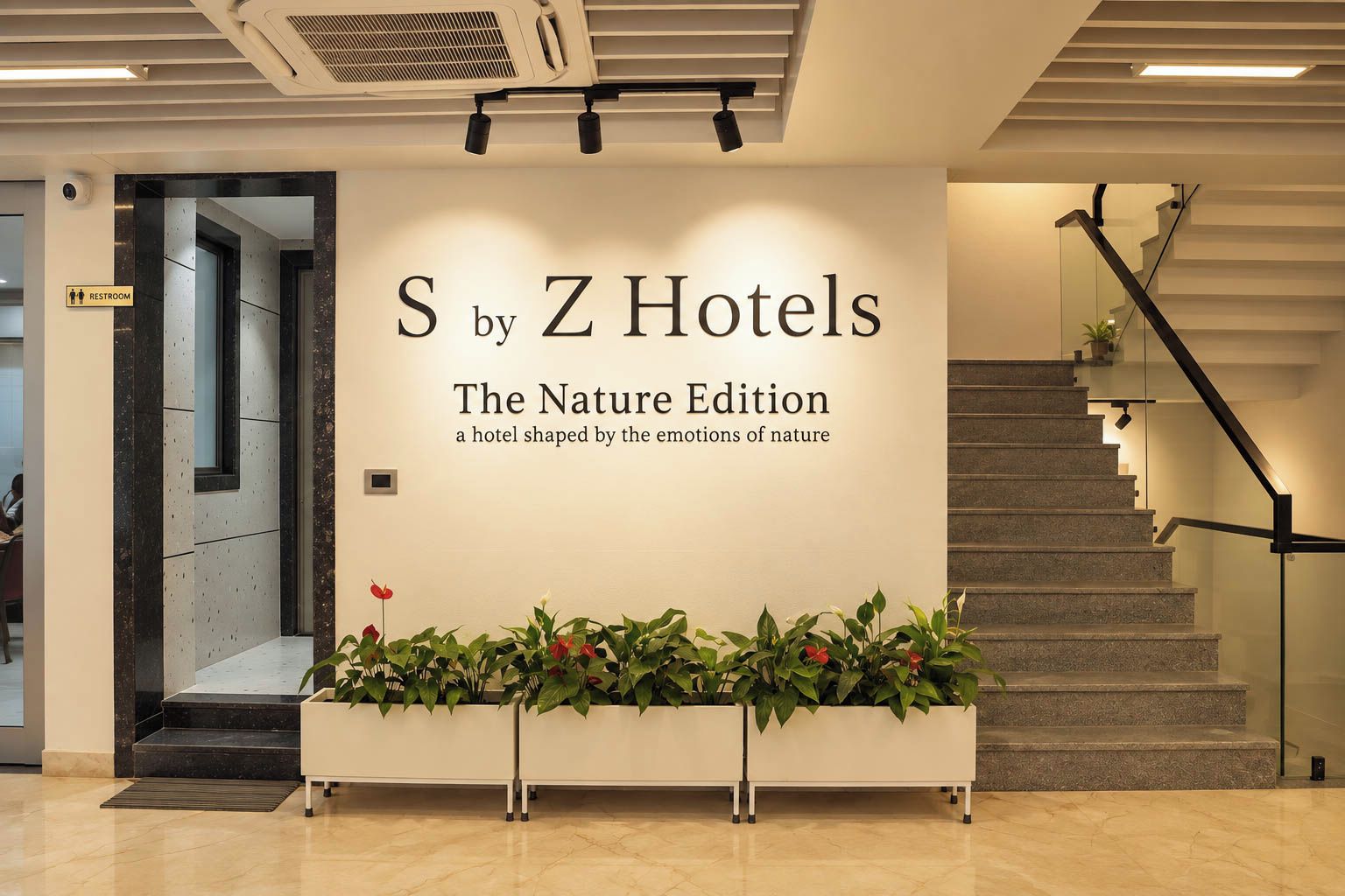 Een receptiezone met een bordje voor 'S by Z Hotels The Nature Edition' en een trap met een glazen balustrade.