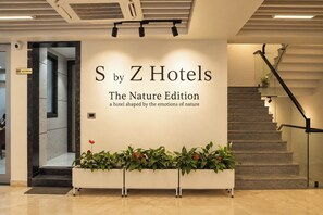 A reception area with a sign for 'S by Z Hotels The Nature Edition' and a staircase with a glass railing. - S by Z Hotels, Baani Square (Gurugram)