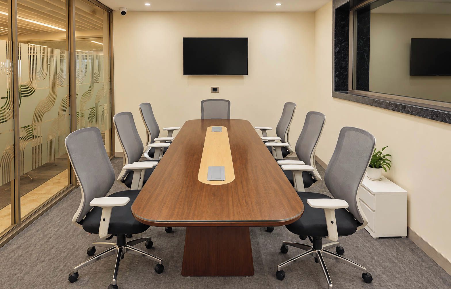 Un salón de conferencias con una mesa larga, varias sillas, un televisor de pantalla plana y una planta en maceta.