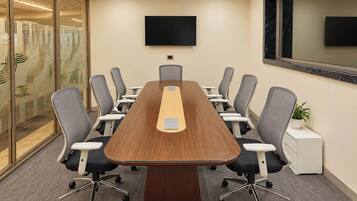 Un salón de conferencias con una mesa larga, varias sillas, un televisor de pantalla plana y una planta en maceta.