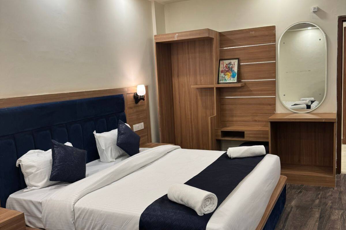 A modern hotel room with a large bed, wooden headboard, and a built-in wardrobe with a mirror.
