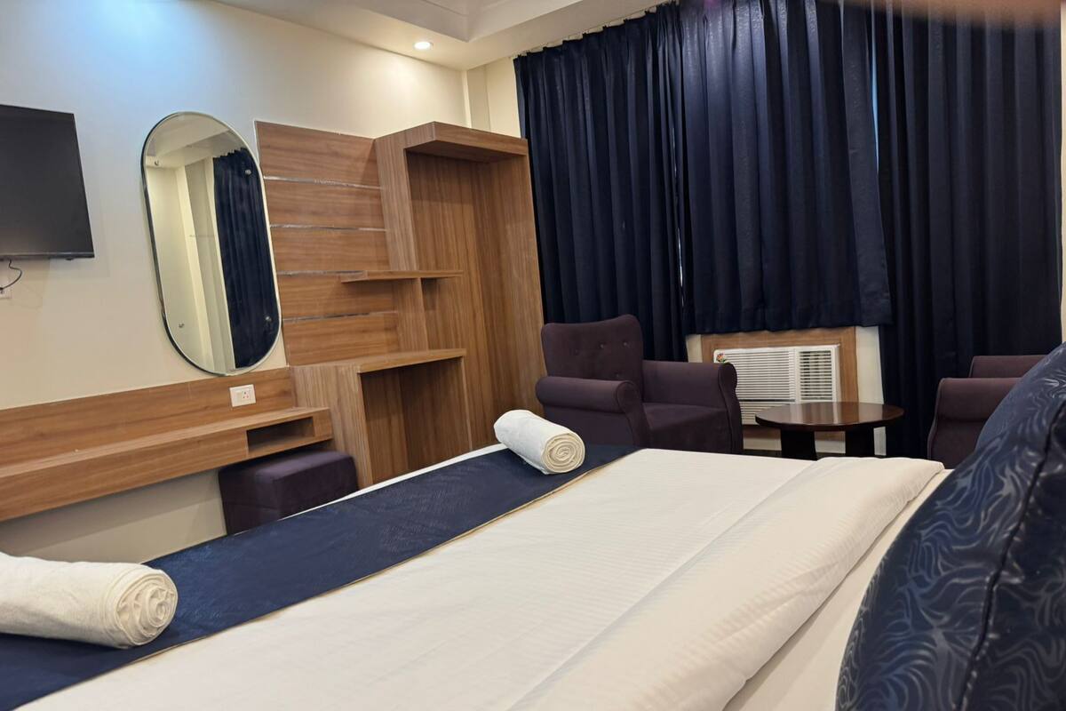 A hotel room with a bed, two armchairs, a small table, a mirror, and a window with curtains.