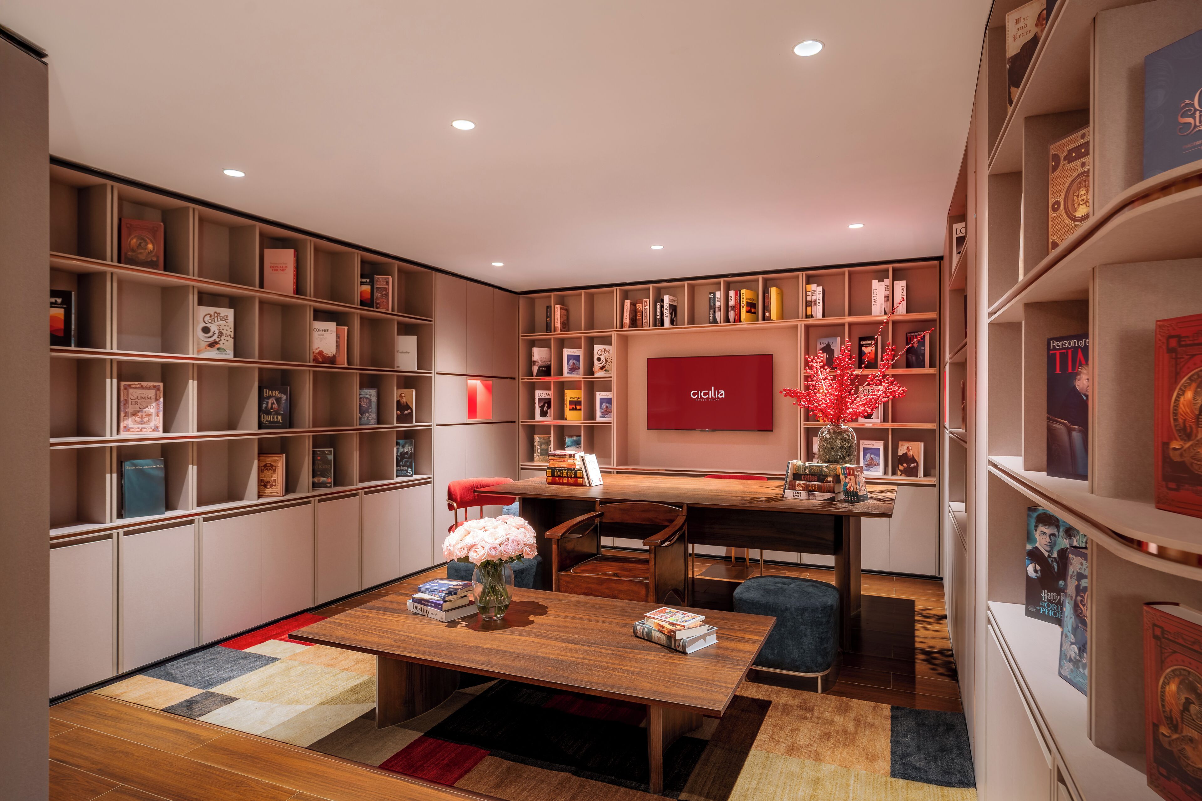 A modern library with bookshelves, a wooden table, and a red wall.