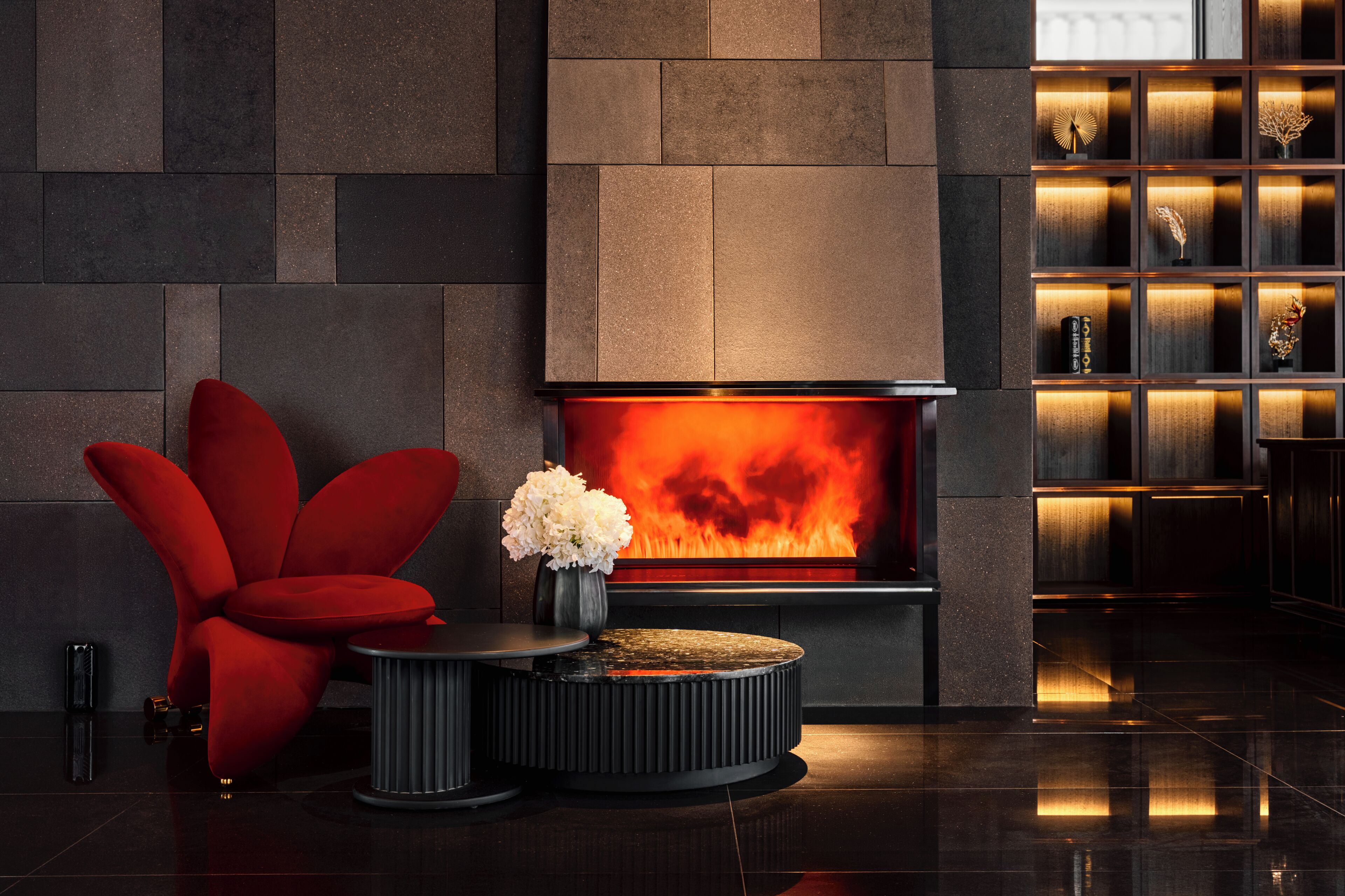 A modern interior with a fireplace, a red chair, and a small table with a vase of flowers.