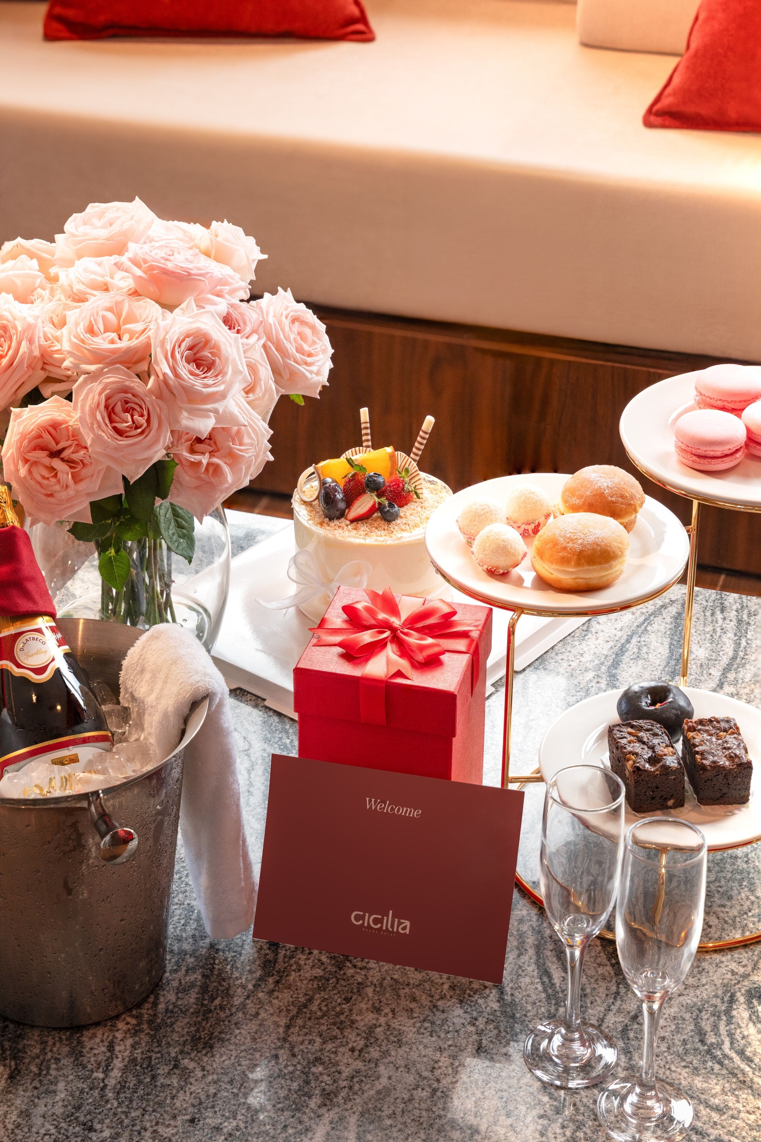 A table with a cake, pastries, a bouquet of roses, a champagne bottle, and a red gift box.