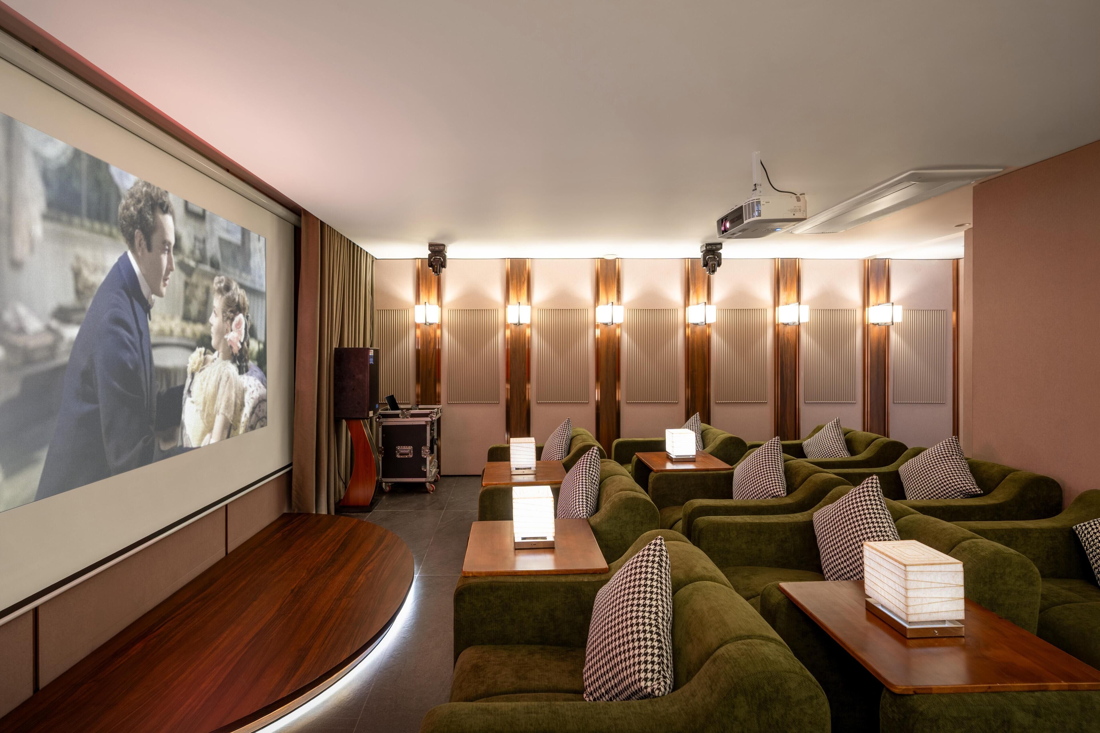 A cinema room with green seating, a screen, and wall-mounted lamps.