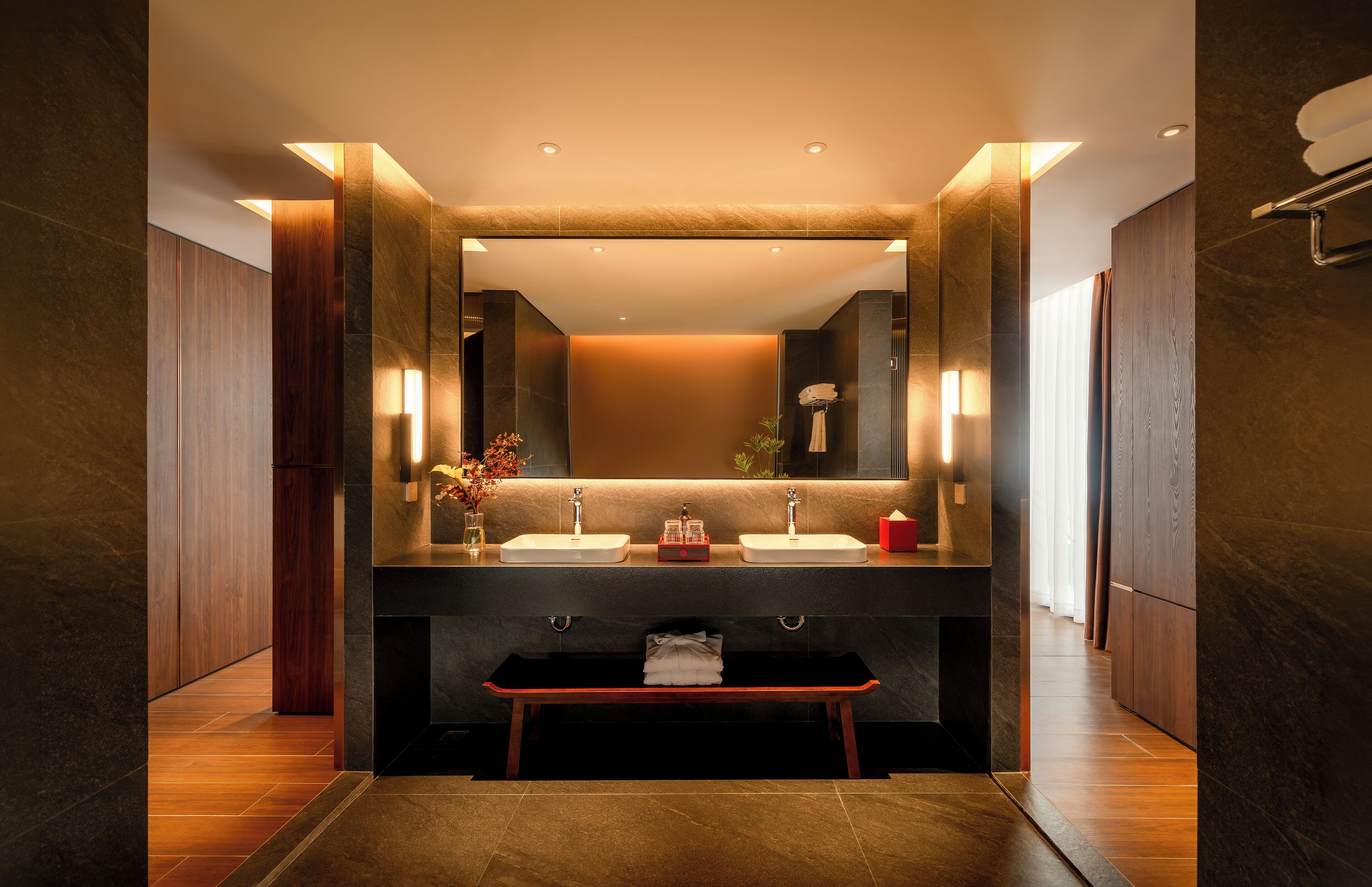 A modern bathroom with two sinks, a bench, and a large mirror.