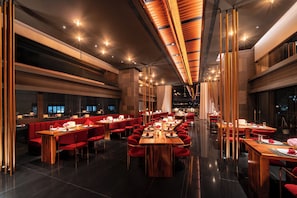 A modern restaurant with multiple dining areas, including long communal tables and individual booths, with a sleek, contemporary design and warm lighting. - Cicilia Rouge Dalat (Da Lat)