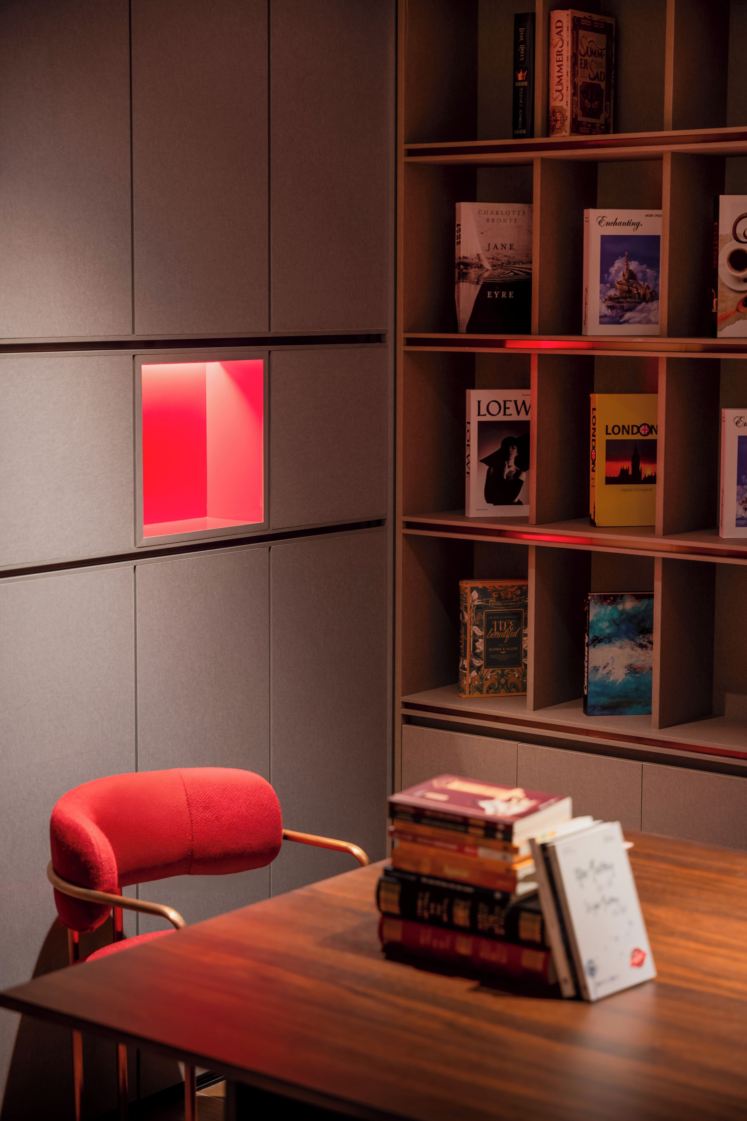 A room with a wooden table, a red chair, and a bookshelf with books.
