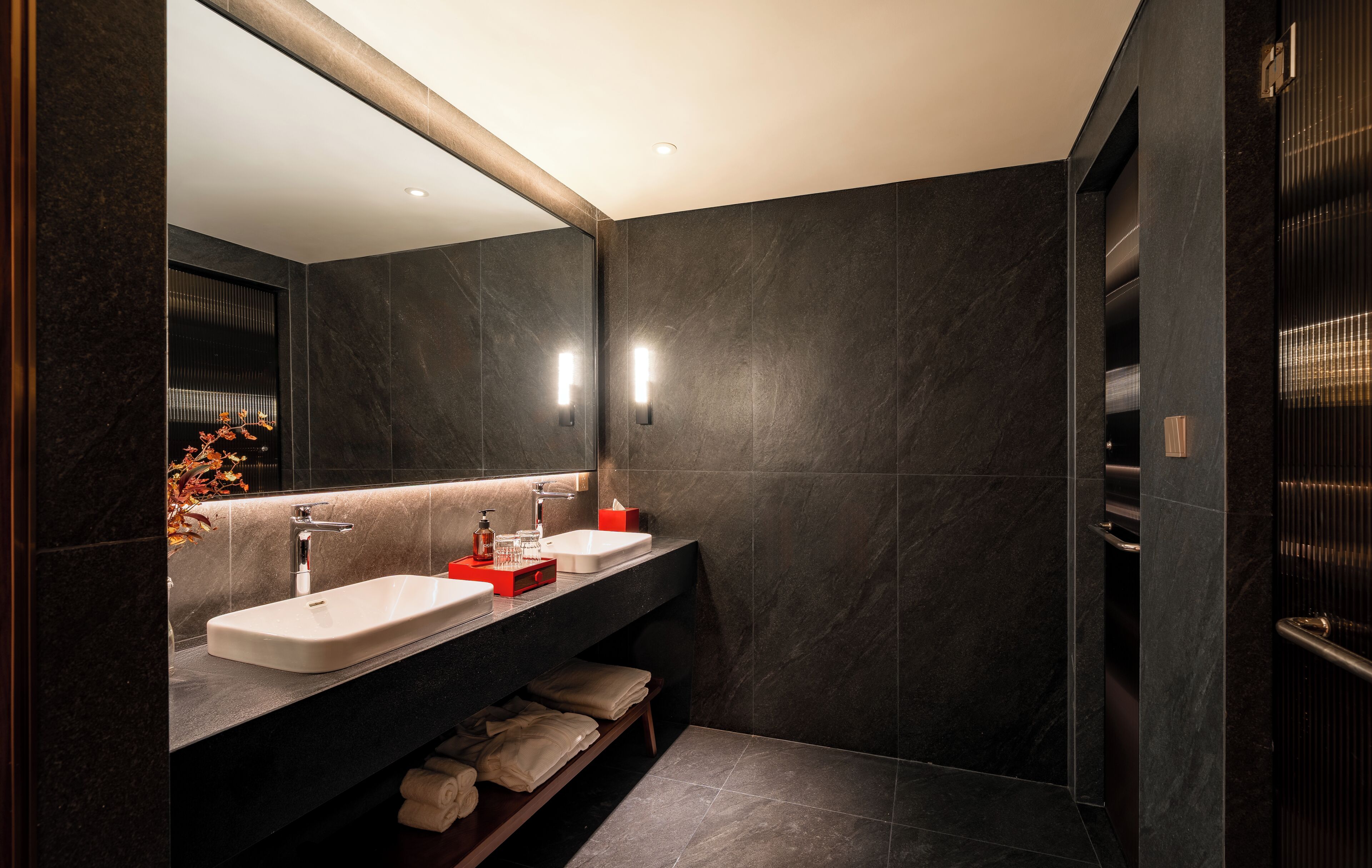 A modern bathroom with a large mirror, two sinks, and a walk-in shower.